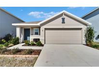 Beige house with gray door, two-car garage, and landscaped yard at 5322 Fiddle Fig Ave, Wimauma, FL 33598