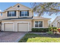 Two-story townhome showcasing neutral stucco, brick driveway, two-car garage, and manicured bushes at 26850 Juniper Bay Dr, Wesley Chapel, FL 33544