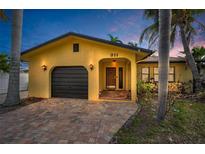Front view of a yellow house with a dark garage door, and a brick driveway at 311 15Th Ave, Indian Rocks Beach, FL 33785