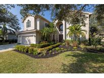 Charming two-story home with a well-manicured lawn, lush landscaping, and a paved driveway leading to an attached garage at 5292 Kernwood Ct, Palm Harbor, FL 34685