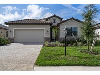 Charming single-story home showcasing stone accents, manicured lawn, and a brick-paved driveway leading to a two-car garage at 11393 Pinot Dr, Venice, FL 34293