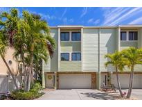 Charming light green townhome featuring a two-car garage, lush tropical landscaping, and a welcoming entrance at 440 Sandy Hook Rd, Treasure Island, FL 33706