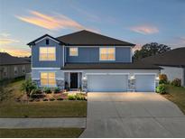 Charming two-story home with a three-car garage, stone accents, and a well-manicured lawn at dusk at 11333 June Briar Loop, San Antonio, FL 33576