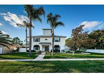 Charming two-story home featuring blue shutters, a manicured lawn, and mature palm trees under a clear blue sky at 614 Maryland Ave, Crystal Beach, FL 34681