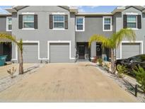 A contemporary two-story townhome features a gray stucco facade, attached garage, and a meticulously landscaped front yard at 33065 Major Oak Dr, Wesley Chapel, FL 33545