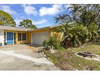 Charming yellow single-story home featuring a blue front door, attached garage, and well-kept landscaping at 1431 54Th Ne Ave, St Petersburg, FL 33703
