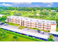 Aerial view of a four-story condo building with golf course views, covered parking, and manicured landscaping at 12200 Vonn Rd # 1305, Largo, FL 33774