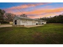 Charming white home featuring large doors, a metal roof, and a spacious green lawn under a beautiful sunset sky at 2040 Underwood Ln, Zephyrhills, FL 33540
