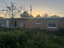 Exterior of run-down house with overgrown plants in the front yard under an orange sunset sky at 5319 Honore Ave, Sarasota, FL 34233