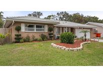 Charming single-story home featuring a well-manicured lawn, lush landscaping, and a unique white tile roof at 5676 Williams Blvd, Seminole, FL 33772