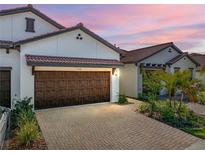 Charming home featuring a brick driveway, two-car garage, and manicured landscaping under a beautiful pink and purple sunset at 17308 Holly Well Ave, Wimauma, FL 33598