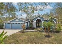 Charming blue home featuring a manicured lawn, arched entry, and a three-car garage at 7546 Richland St, Wesley Chapel, FL 33544