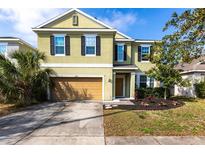 Two-story home featuring a two-car garage, well-maintained lawn, and freshly planted shrubbery under a clear, blue sky at 11539 Tangle Branch Ln, Gibsonton, FL 33534