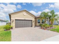 Tan single-story home featuring a brick driveway, a two-car garage and tropical landscaping at 4920 Sevilla Shores Dr, Wimauma, FL 33598