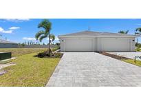 Modern home showcasing a paved driveway leading to a two-car garage with manicured lawn and tropical landscaping at 8069 Shore Lake Dr, Englewood, FL 34224