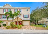 Exterior view of a three story townhome with a red door, one car garage, and landscaped front yard at 876 Callista Cay Loop, Tarpon Springs, FL 34689