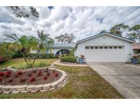 Charming home featuring a two-car garage, blue shutters, and a meticulously landscaped front yard with beautiful flowerbeds at 2086 Whitney N Pl, Clearwater, FL 33760