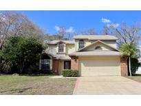 Two-story tan home featuring a brick facade, attached two-car garage, and beautifully landscaped front yard at 6307 Songbird Way, Tampa, FL 33625