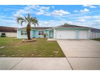 Inviting turquoise home with a two-car garage, well-kept lawn, and beautiful palm tree at 11248 Andy Dr, Riverview, FL 33569