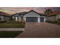 Gray-toned house with gray garage doors, landscaping, and brick paver driveway at dusk at 11061 Egeria Dr, Odessa, FL 33556