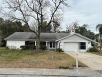 One-story house with white brick exterior, attached garage, and mature landscaping at 8611 Wagon Wheel Ln, Hudson, FL 34667