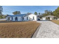 White single-story home with gray roof, paver driveway, and detached barn at 9331 Elida Rd, Spring Hill, FL 34608