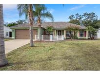 Green house with brown garage door, white fence, and palm trees in the front yard at 3497 Chadwick Ave, Spring Hill, FL 34609