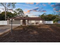 Single-story house with a brown roof, white fence, and a well-maintained lawn at 7489 Gates Cir, Spring Hill, FL 34606