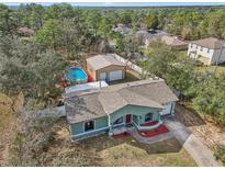 Aerial view of a light green house with a large pool, big detached garage and mature trees at 13083 Jaywalk Rd, Brooksville, FL 34614