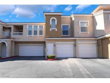 Tan two-story townhouse with white garage doors and landscaping at 10001 Peace Way # 2324, Las Vegas, NV 89147