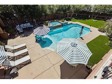 Aerial view of a backyard pool and spa area surrounded by lounge chairs, striped umbrellas, and artificial turf at 6391 Tempting Choice Ave, Las Vegas, NV 89131