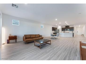 Spacious open-concept living area with modern gray flooring, a brown leather sofa, and a coffee table at 3540 Valley Lily St, North Las Vegas, NV 89032