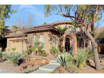 Tan two-story house with a three-car garage, landscaping, and a curved entryway at 178 Uccello Dr, Las Vegas, NV 89138