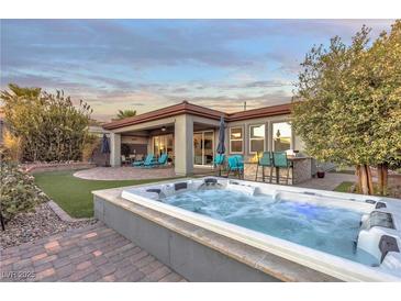 Luxurious backyard featuring a hot tub, covered patio, outdoor kitchen, and well-manicured landscaping at 138 Reflection Cove Dr, Henderson, NV 89011