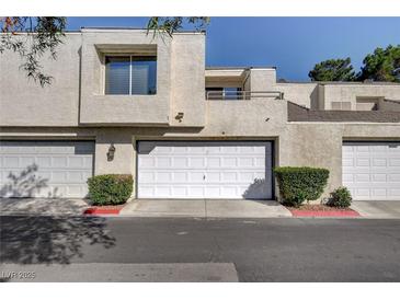 Tan stucco exterior of townhome with white garage doors and landscaping at 8945 Clairton Ct, Las Vegas, NV 89117