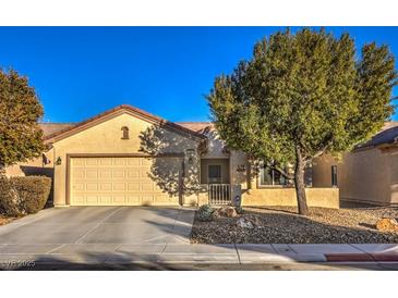 Single-story house with a beige exterior, two-car garage, and landscaped front yard at 7824 Homing Pigeon St, North Las Vegas, NV 89084