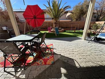 Inviting backyard with a patio table, seating area, and a fun playset with lush green grass at 11173 Varedo Ct, Las Vegas, NV 89141