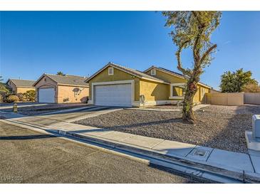 Tan one-story house with a white garage door and landscaping at 2210 Cool River Ct, North Las Vegas, NV 89032