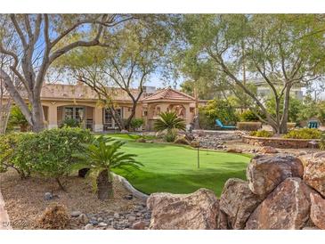 Beautiful backyard putting green featuring mature trees, desert landscaping and covered structure at 7450 Via Olivero Ave, Las Vegas, NV 89117