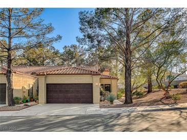 Tan stucco house with brown garage door, and mature trees at 7923 Canoe Ln, Las Vegas, NV 89145