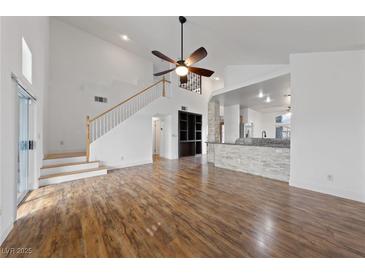 Bright living room with wood floors, high ceilings, ceiling fan, and view of the open-concept kitchen and staircase at 319 Horse Pointe Ave, North Las Vegas, NV 89084