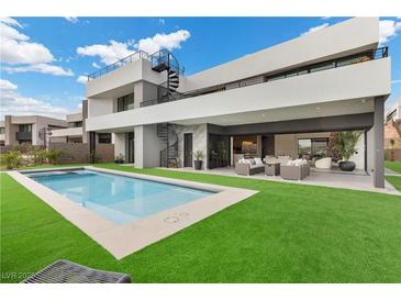 An expansive backyard shows a modern pool, well manicured grass, outdoor seating, and access to a spiral staircase at 21 Canyon Bay Dr, Henderson, NV 89011