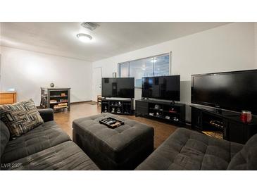 Open living room with wood floors, gray sofa, large window, and three large televisions at 271 Greenbriar Townhouse Way, Las Vegas, NV 89121