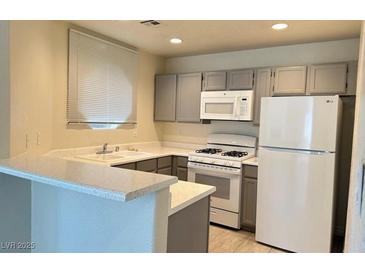Modern kitchen featuring gray cabinets, white appliances, and a breakfast bar at 5002 S Rainbow Blvd # 106, Las Vegas, NV 89118
