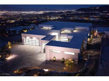 Stunning modern home with clean lines, expansive windows, and a spacious driveway featuring a striking city view at night at 658 Dragon Peak Dr, Henderson, NV 89012