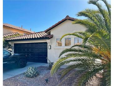 Charming single-story home featuring a black garage door, red tile roof, and desert landscaping at 9995 Yellow Canary Ave, Las Vegas, NV 89117