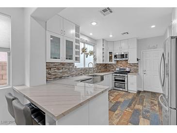 Bright kitchen featuring white cabinets, stone countertops, stainless steel appliances, and stylish backsplash at 11908 Love Orchid Ln, Las Vegas, NV 89138