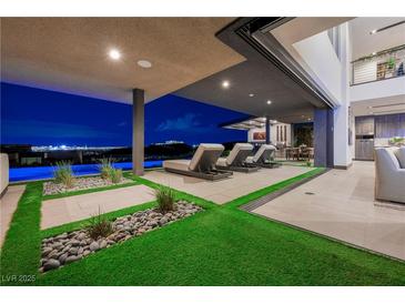 Modern outdoor living space featuring lounge chairs, lush landscaping, and stunning city views beyond the pool at 1786 Diamond Rim Ct, Henderson, NV 89012