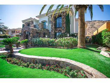 Beautiful two-story home featuring a lush lawn, colorful flowerbeds, and mature palm trees at 2793 Red Arrow Dr, Las Vegas, NV 89135