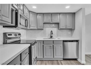 Updated kitchen features grey cabinetry, white countertops, marble backsplash, and stainless steel appliances at 808 N Torrey Pines Dr, Las Vegas, NV 89107
